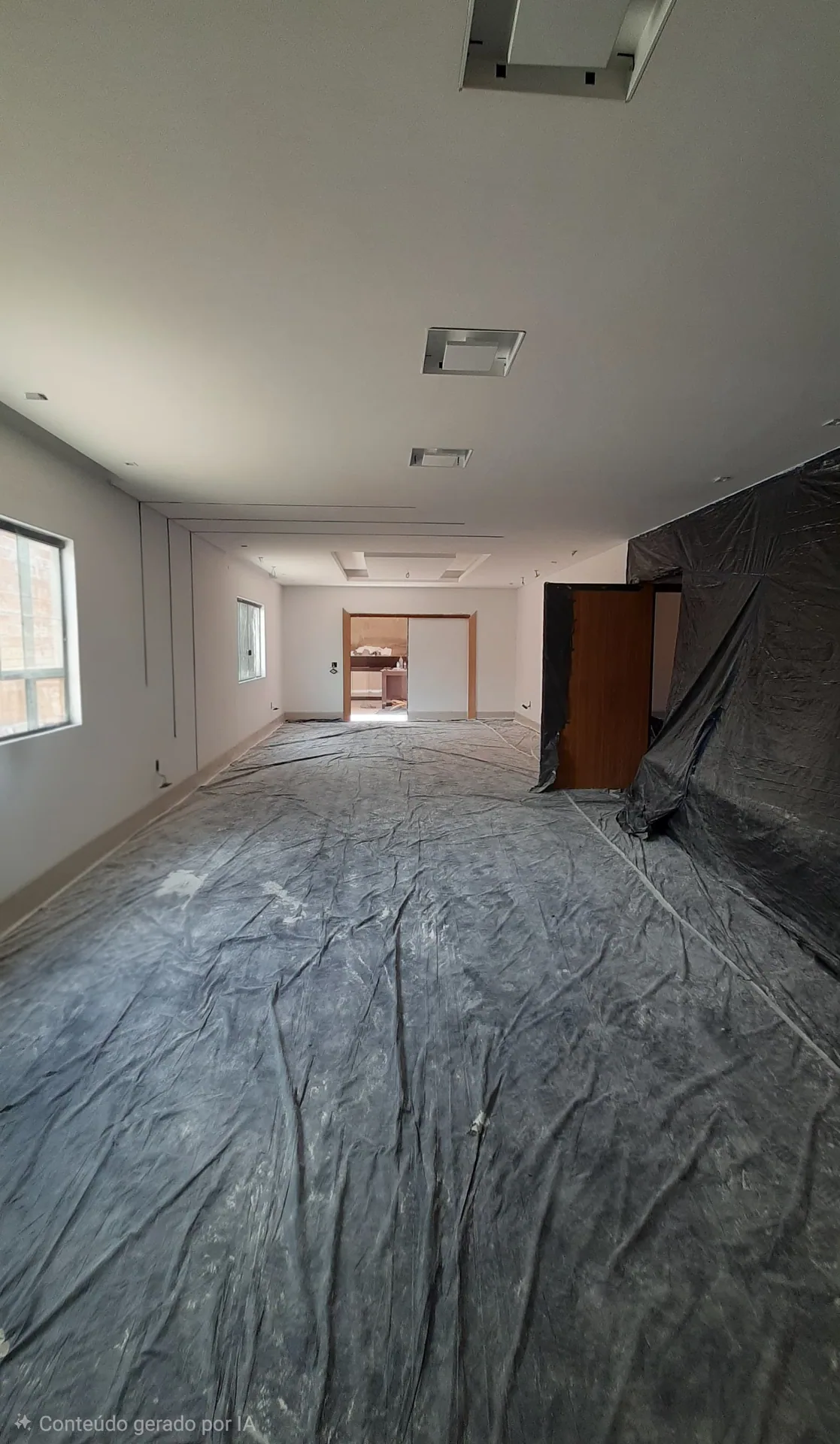 O salão pronto: paredes lisas e pintadas, forro de gesso liso com rebaixos e alçapões quadrados, porta de madeira ao fundo e o piso ainda coberto com lona