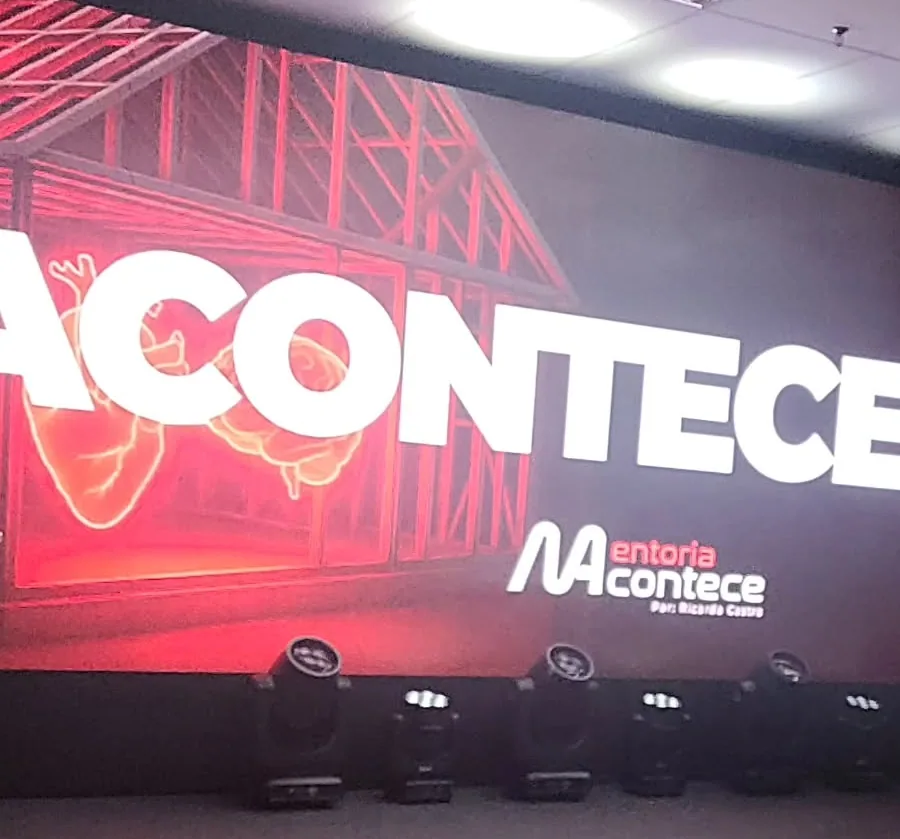 Palco de um evento de steel frame em São Paulo: telão vermelho com o desenho da estrutura de uma casa e o nome do evento, refletores no chão