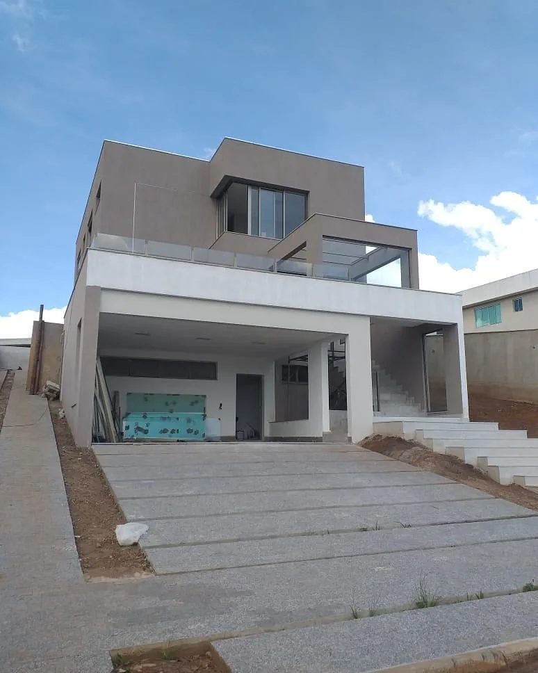 Casa na Península dos Pássaros, em Alphaville: fachada de dois andares em cinza e branco, garagem coberta, guarda-corpo de vidro e rampa de pedra na entrada